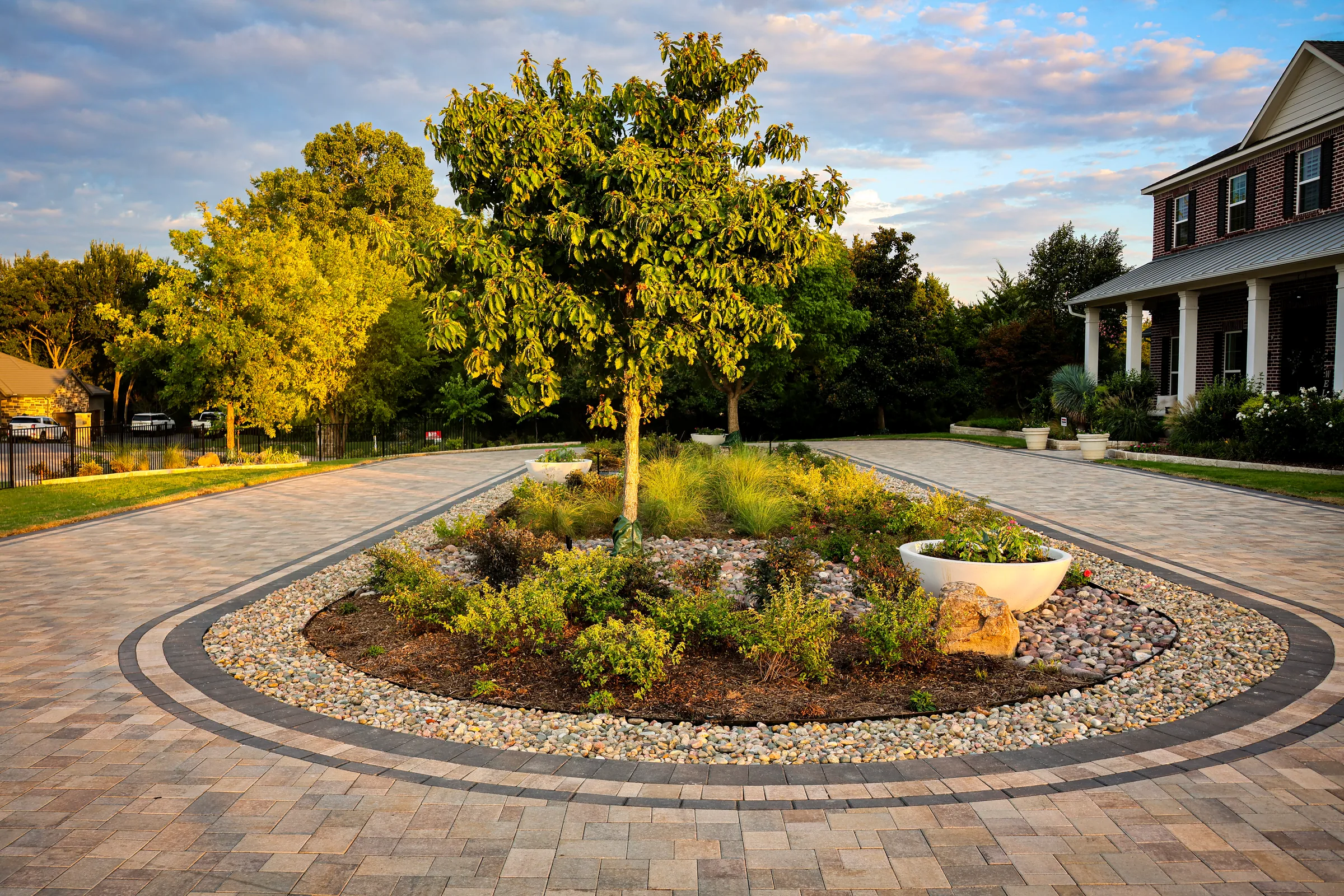 Paver driveway circling a landscaped garden island with a mature tree
