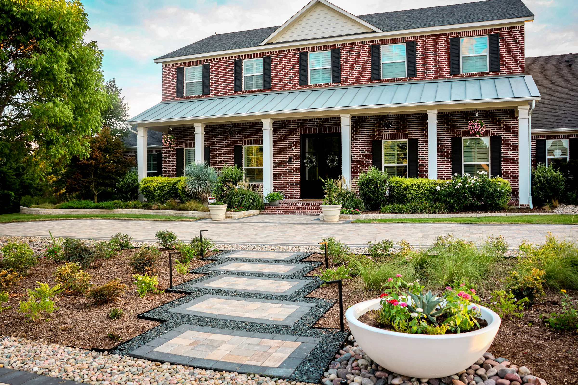 Square paver stepping pads crossing a planted island toward a brick home