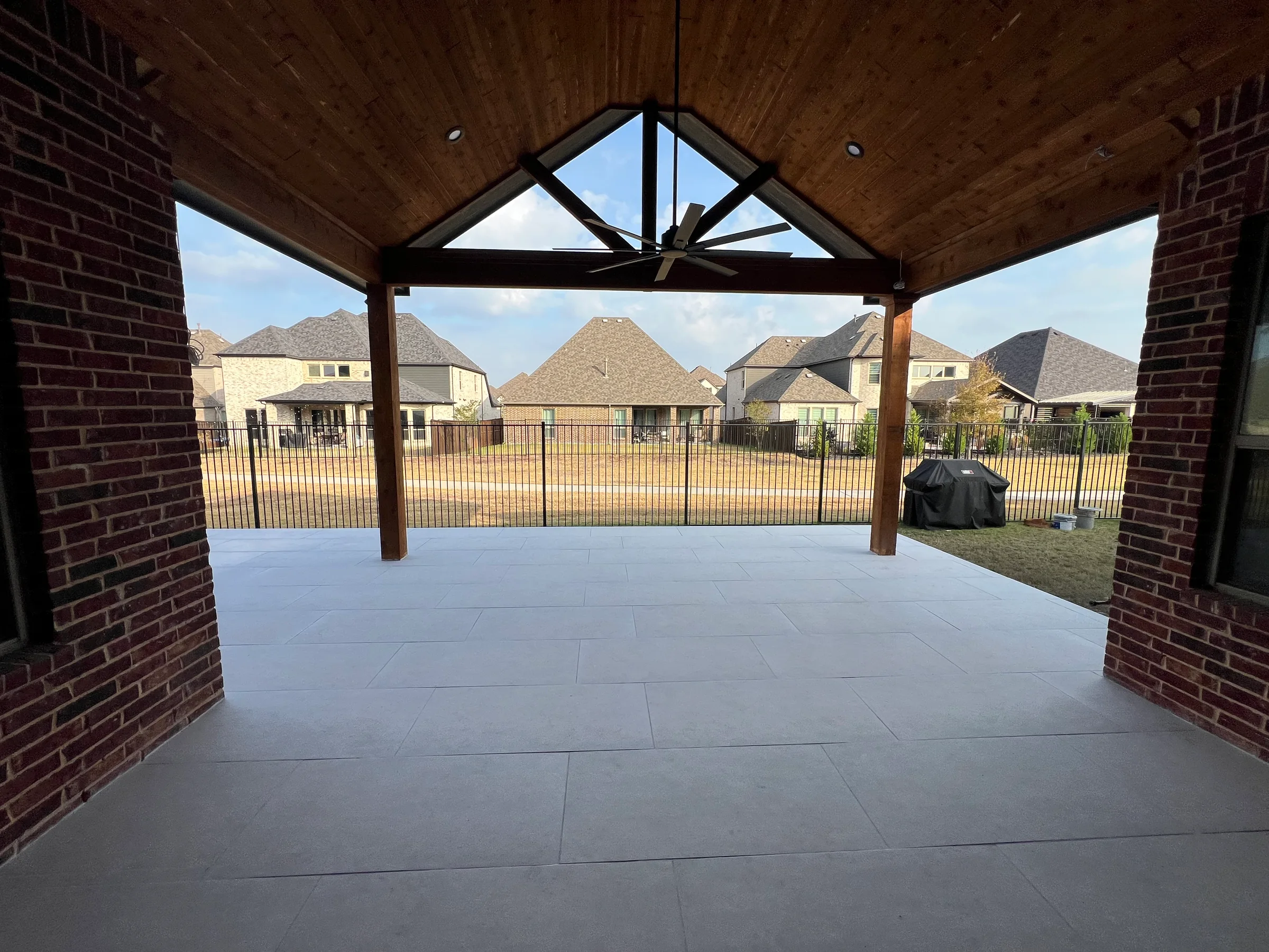 Completed covered residential patio with wood ceiling, ceiling fan, brick columns, and large-format paver flooring