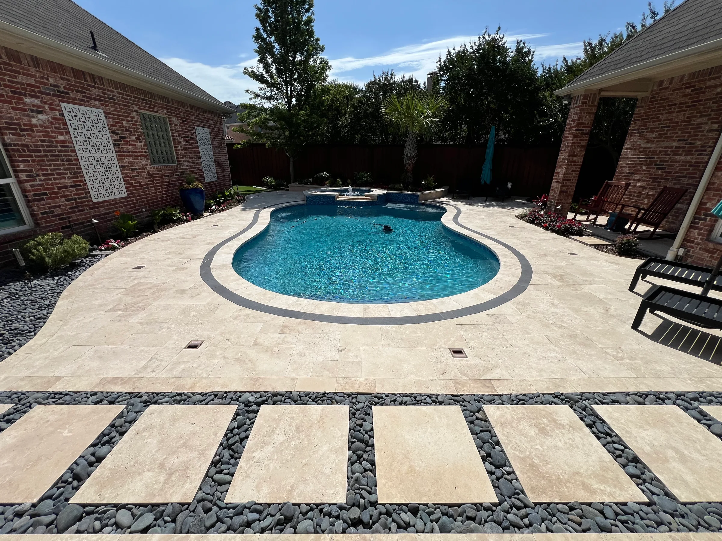 Completed residential pool and surrounding travertine-style patio with decorative stone landscaping and stepping-stone walkway