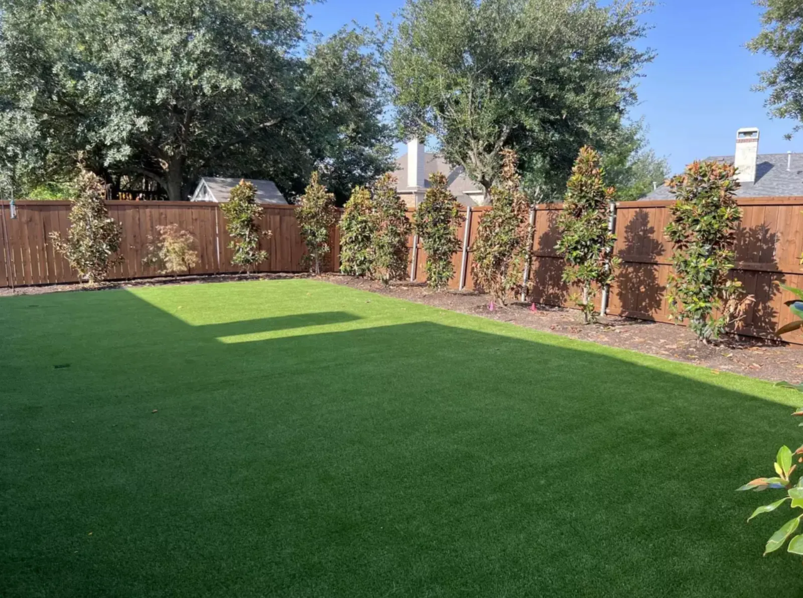 Finished artificial turf lawn framed by a wood fence and new planting