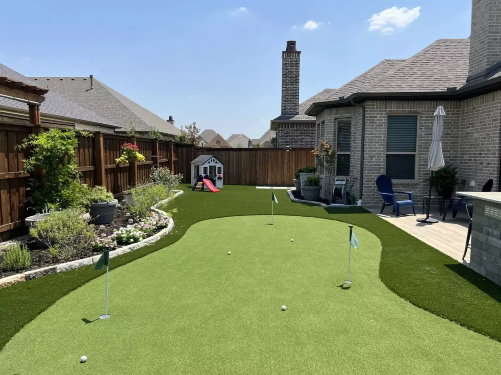Wide view across a contoured backyard putting green toward a covered patio