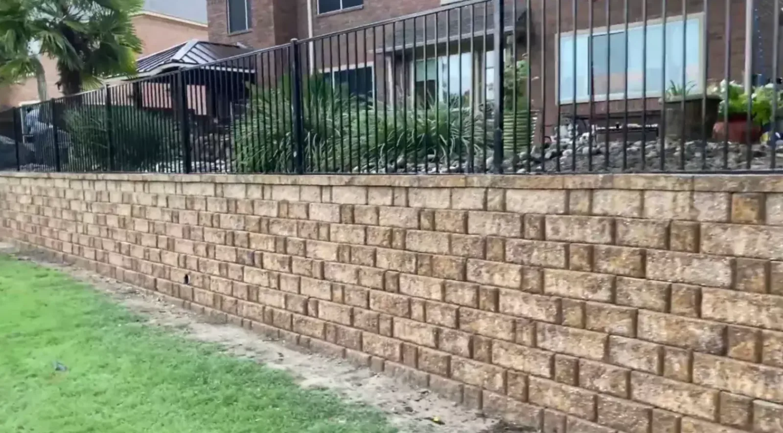 Long block retaining wall supporting an elevated lawn beside a home