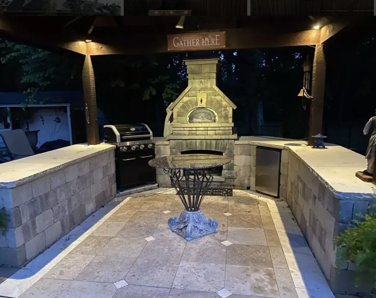 Covered outdoor kitchen with stone counters, built-in grill, and paver flooring