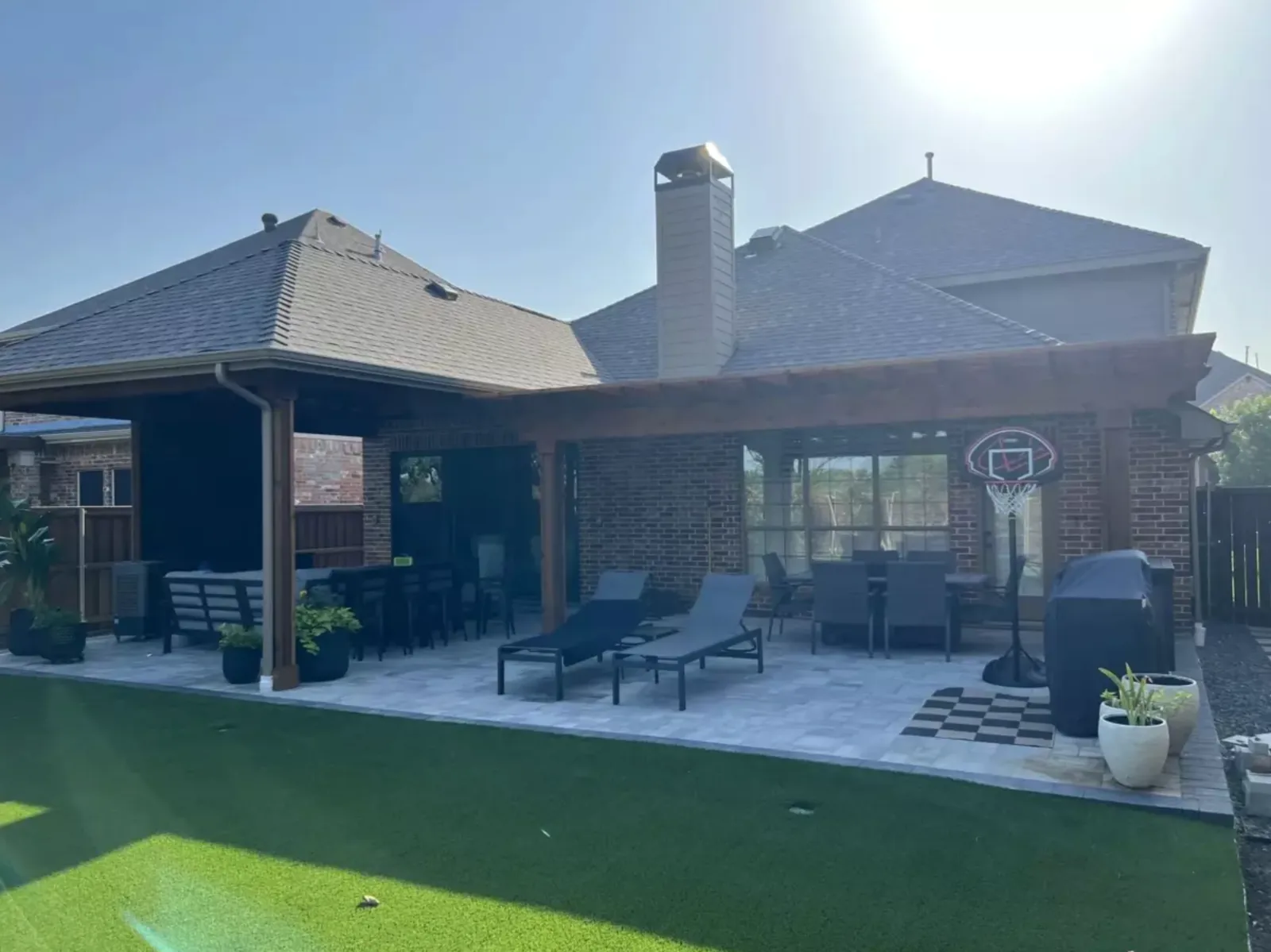 Covered backyard patio opening onto a broad artificial turf lawn