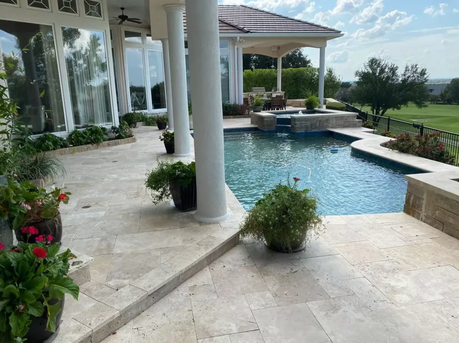 Light stone pool deck connecting a covered patio to a backyard swimming pool