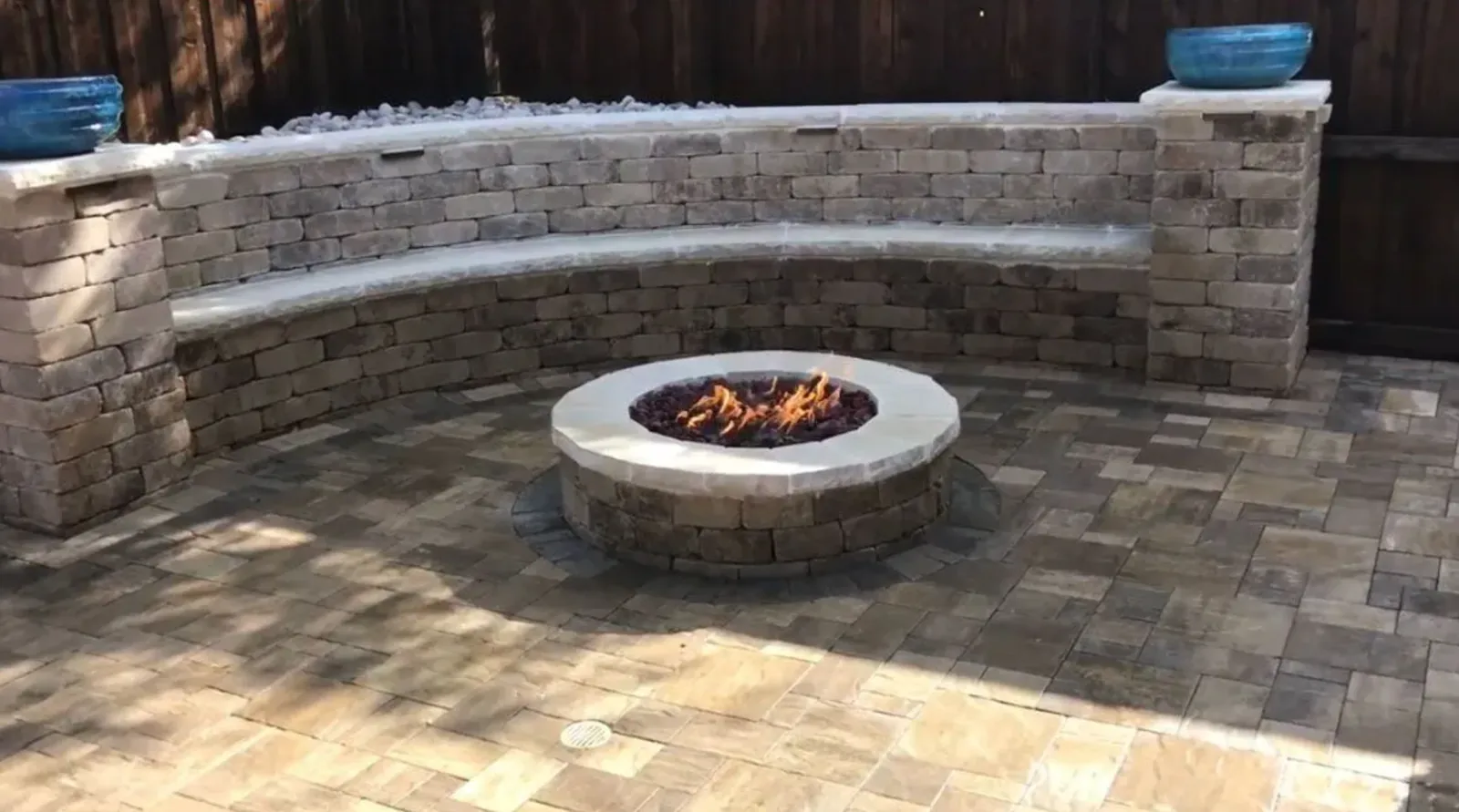 Round fire pit centered within a curved two-tier stone seat wall
