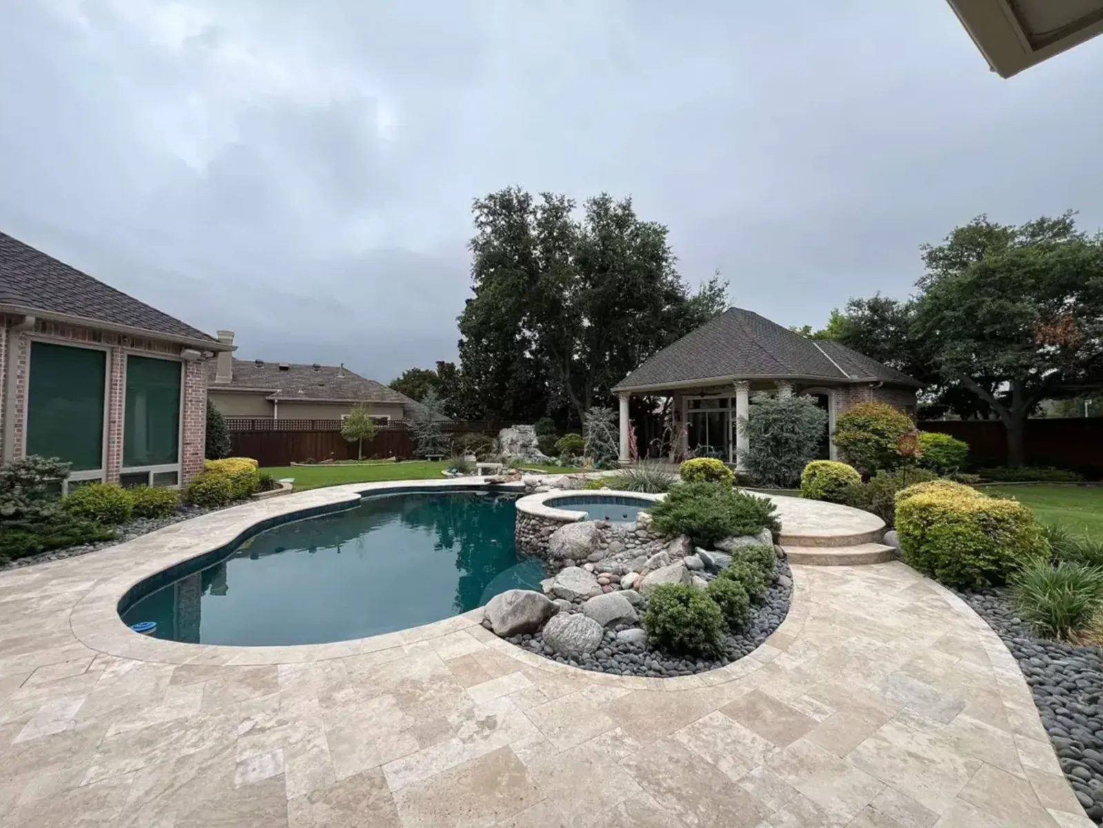 Curving light stone pool deck surrounding a freeform backyard swimming pool