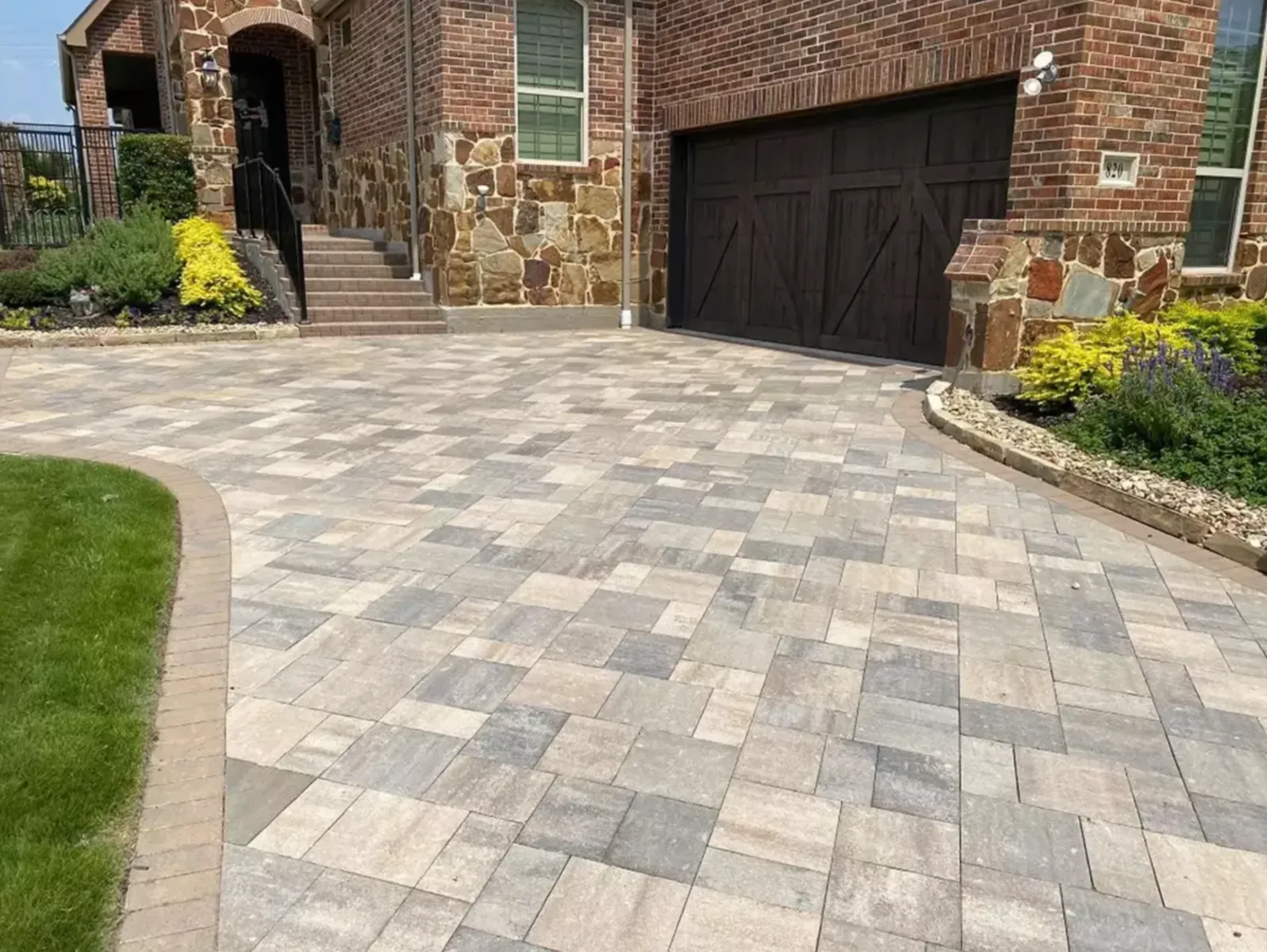 Curved multicolor paver driveway meeting a stone-edged front entry