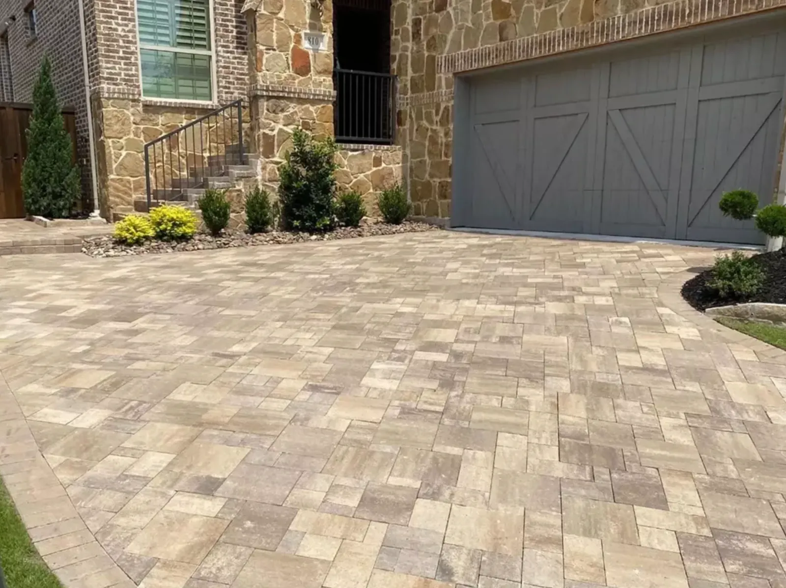 Multicolor paver driveway laid across the front of a stone and brick home