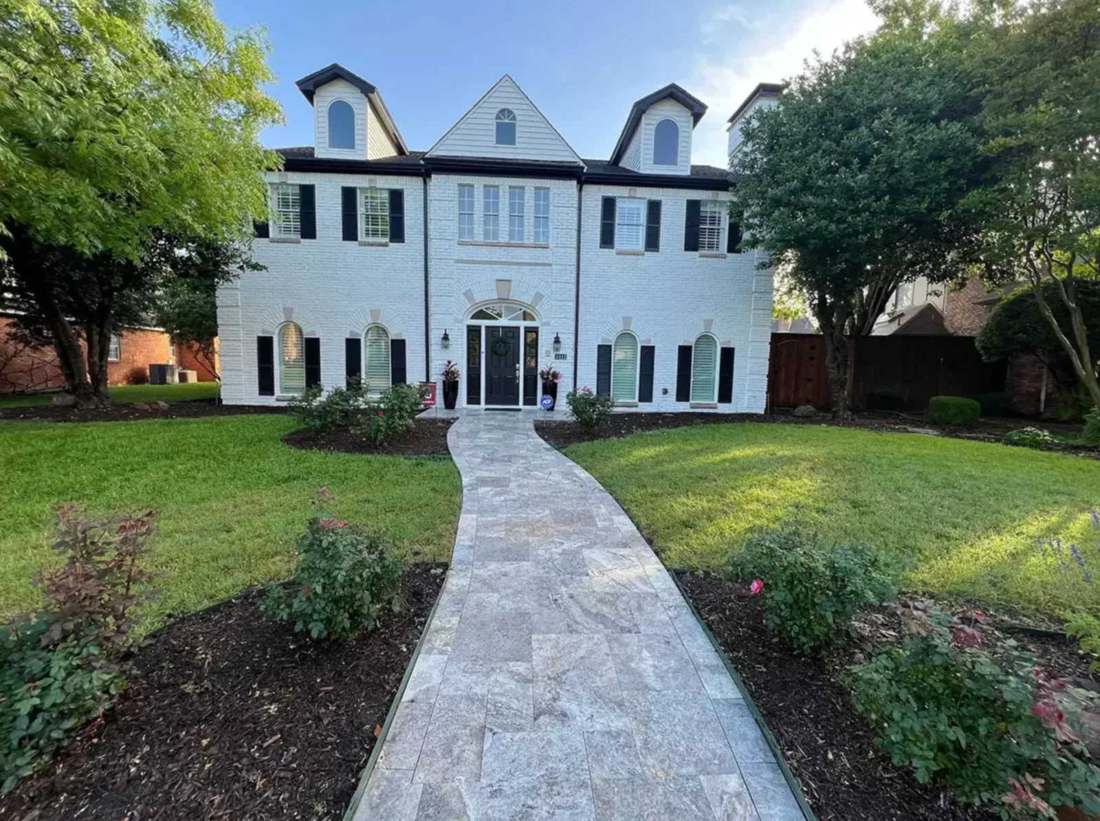 Straight formal paver walkway leading across a lawn to a white home