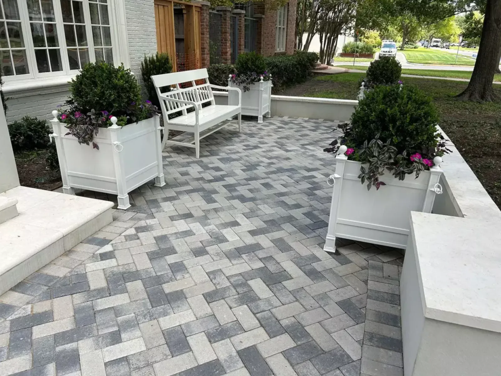 Patterned paver courtyard with white planters and built-in seating near a front entry