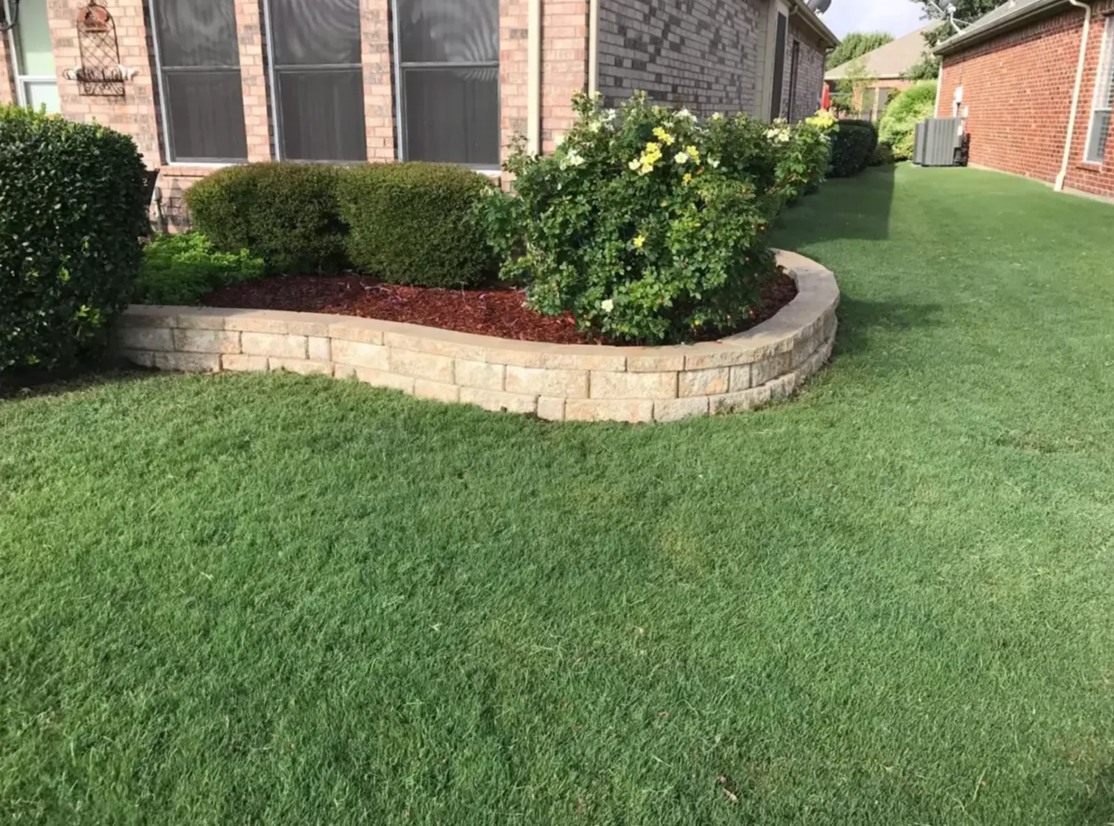 Artificial turf lawn meeting a curved stone planter wall in a front yard