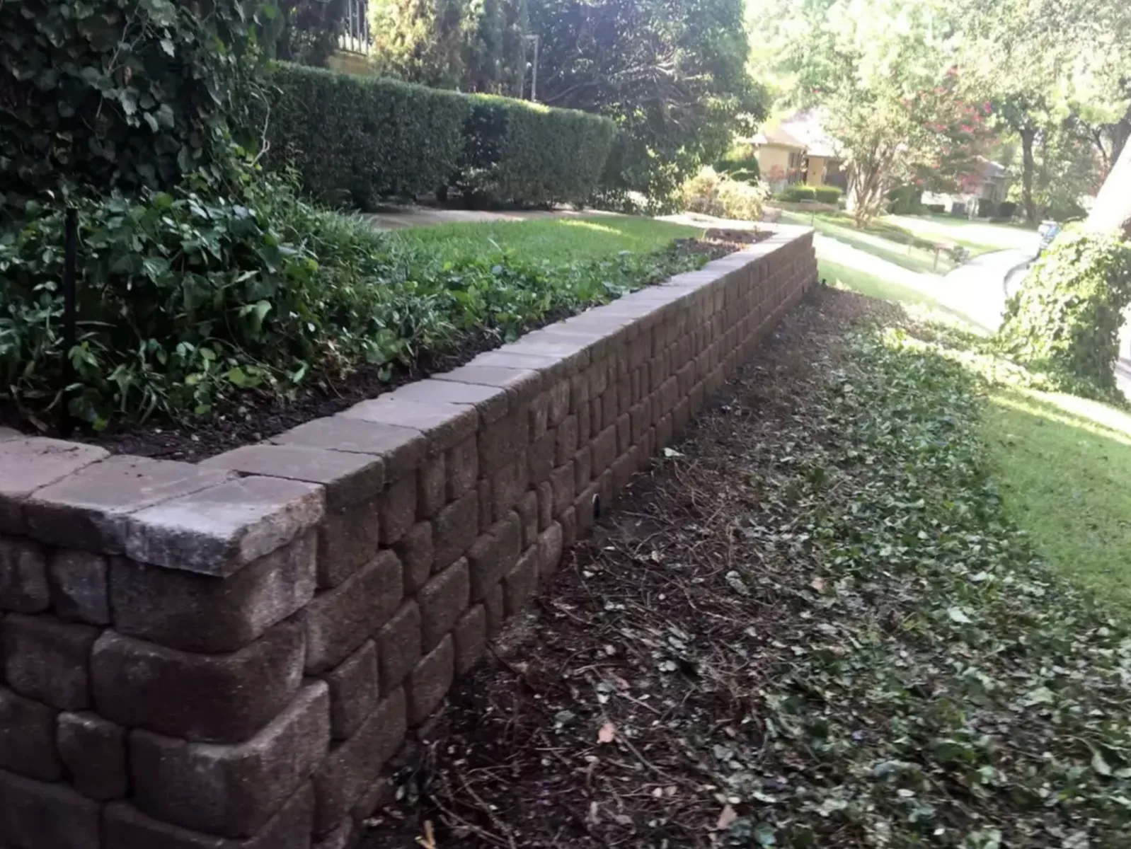 Low garden retaining wall following the slope of a landscaped front yard