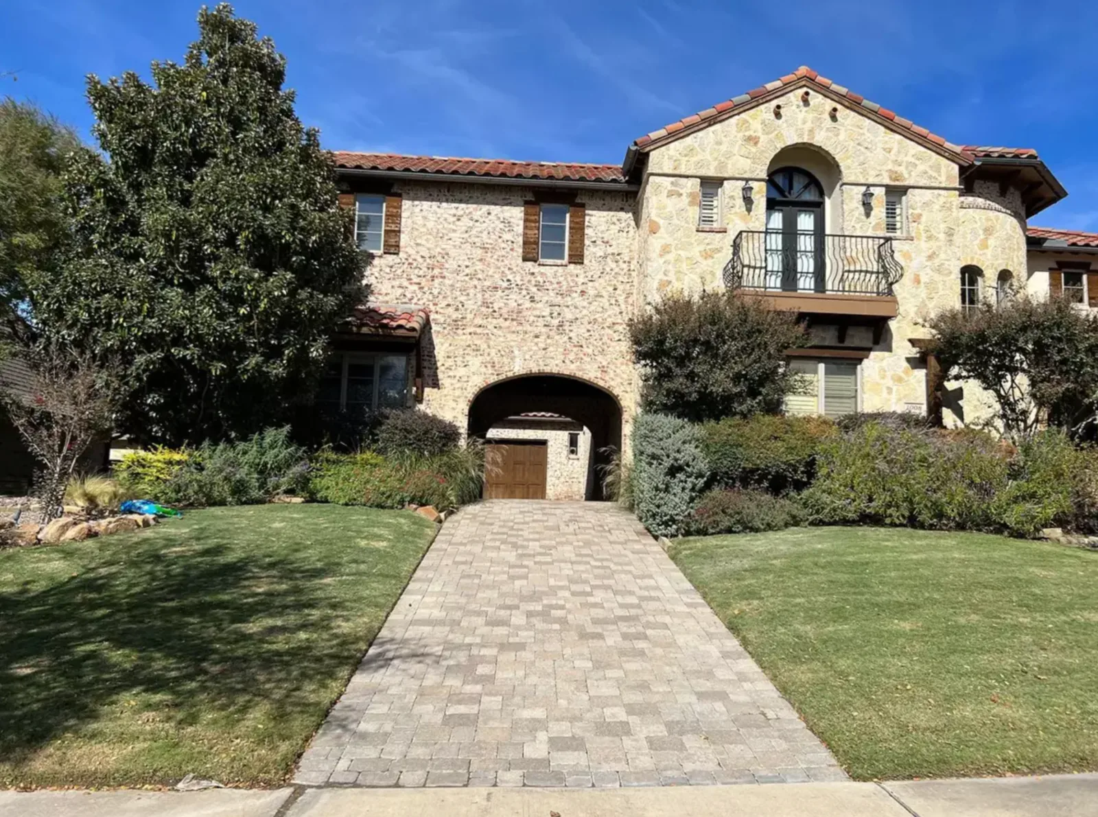Curved paver walkway leading through a landscaped front yard to a Mediterranean-style home