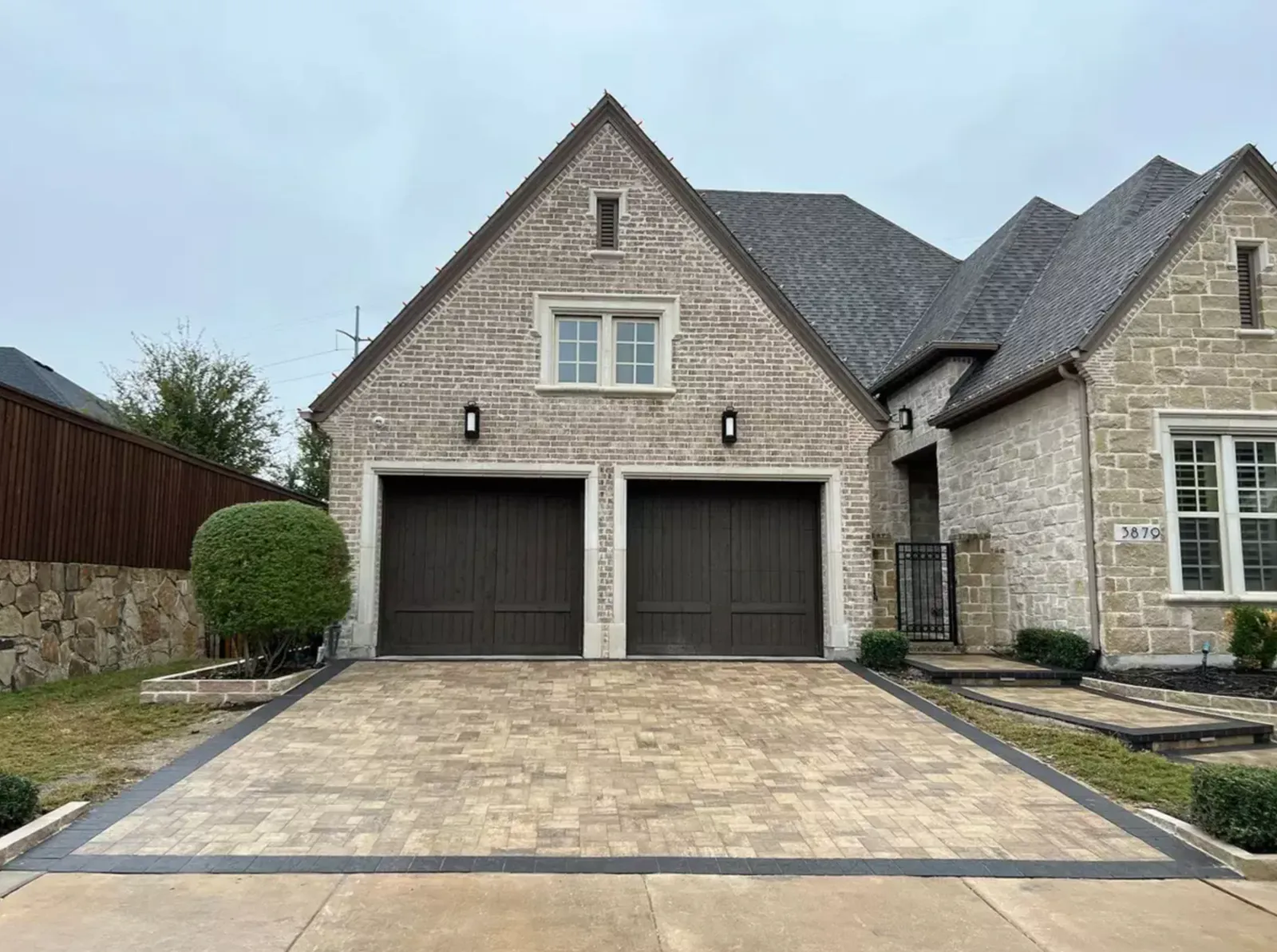 Modern light paver driveway with a dark border in front of a brick home