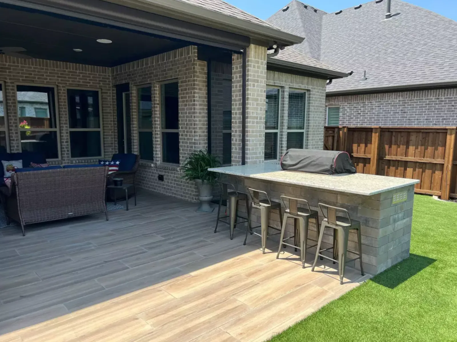 Stone outdoor kitchen beside a covered patio and backyard putting green