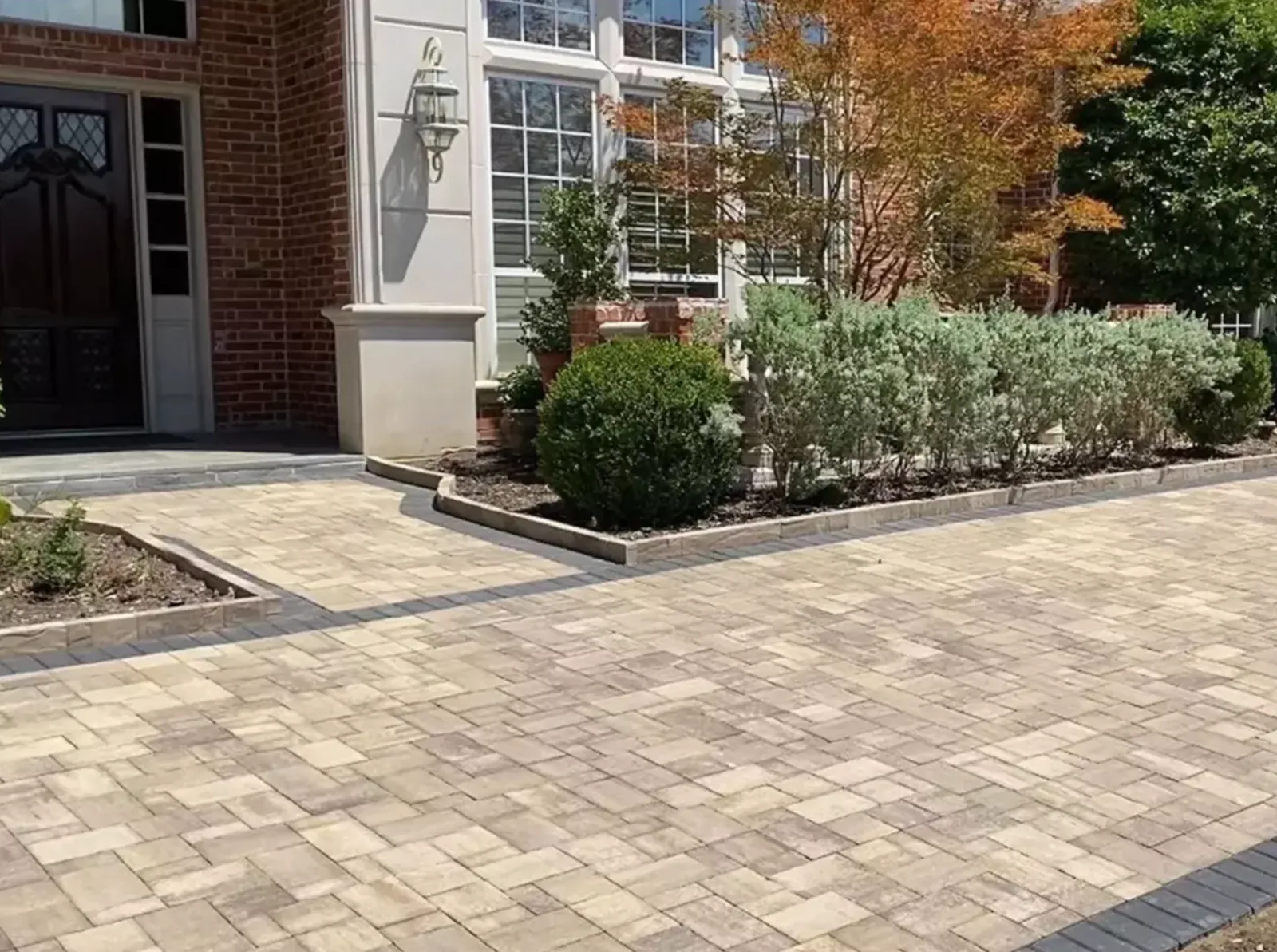 Large paver courtyard with planting beds beside a brick home