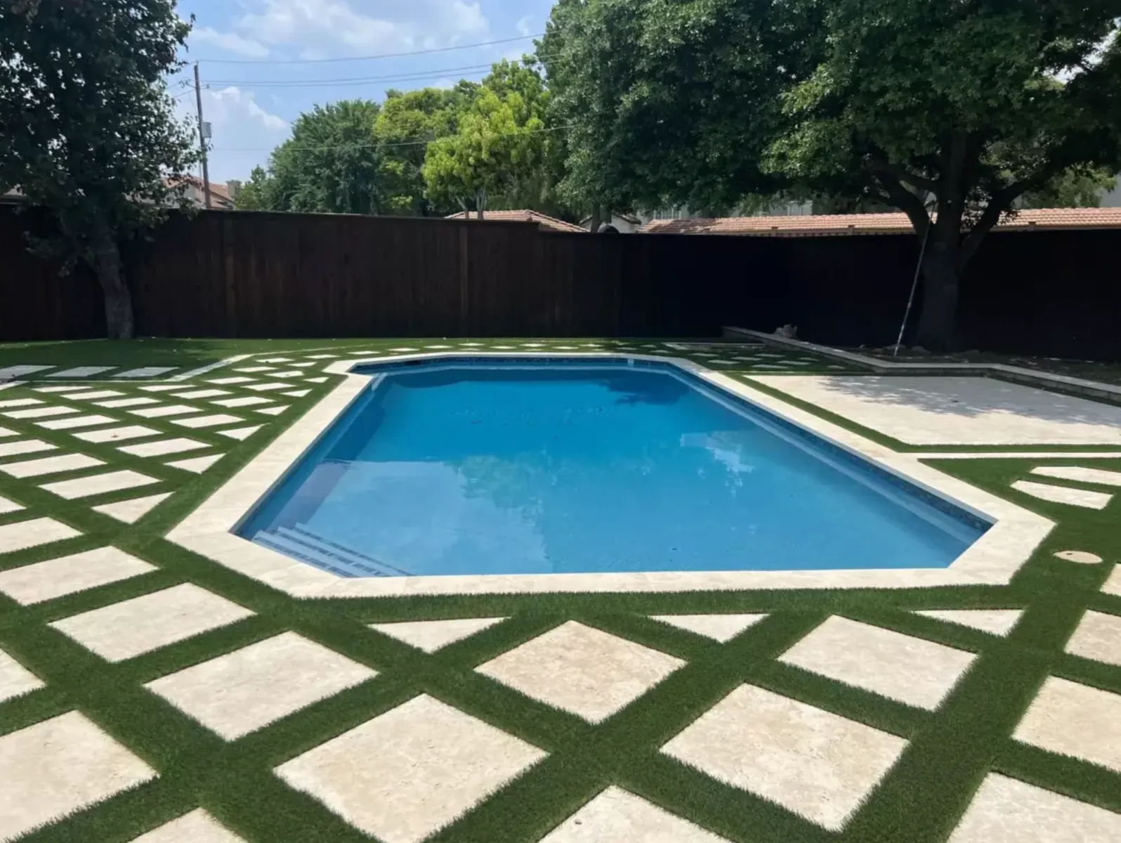 Wide view of a swimming pool framed by a geometric stone and turf deck
