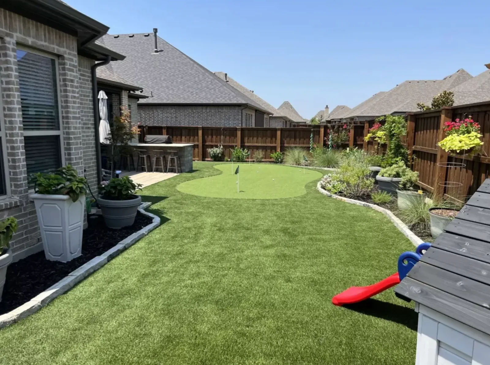 Contoured backyard putting green beside an outdoor kitchen and planting beds