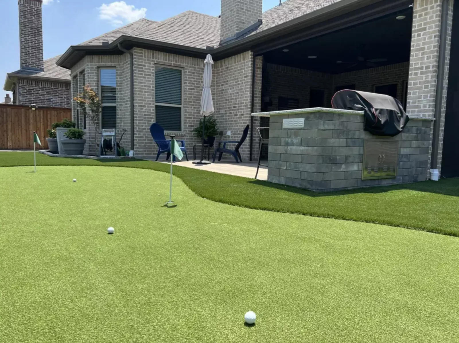 Backyard putting green curving past a stone outdoor kitchen