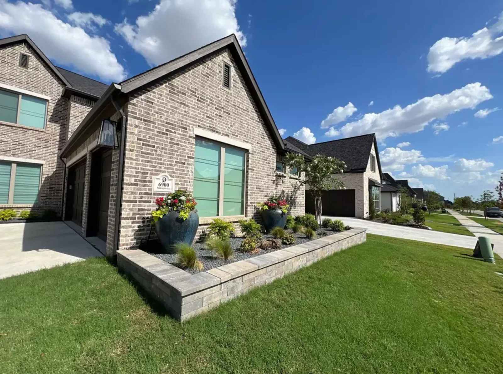 Artificial turf lawn beside a raised stone planter at a brick home