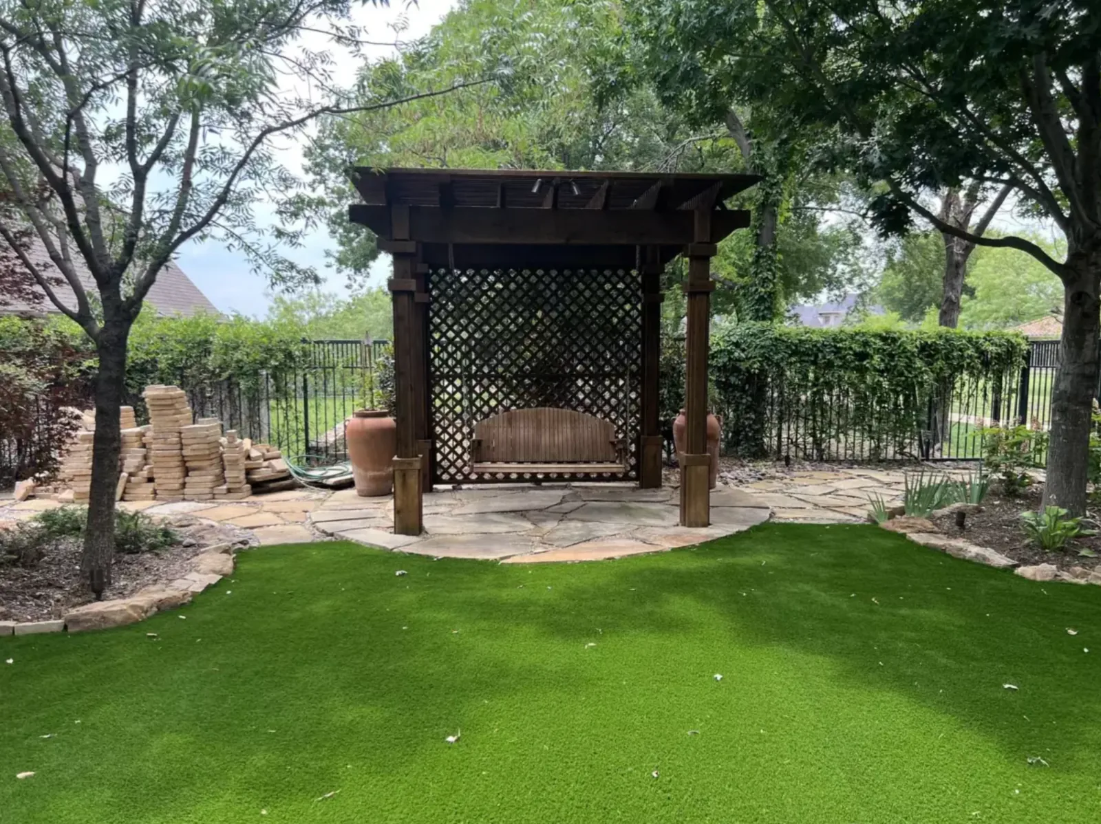 Artificial turf gathering area beneath mature trees beside a wood pergola