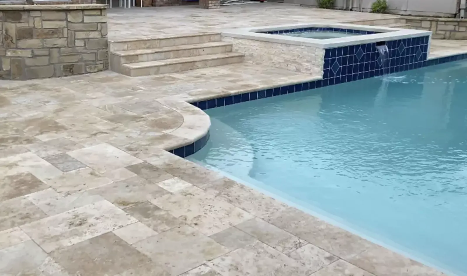 Light stone pool deck and steps meeting blue waterline tile