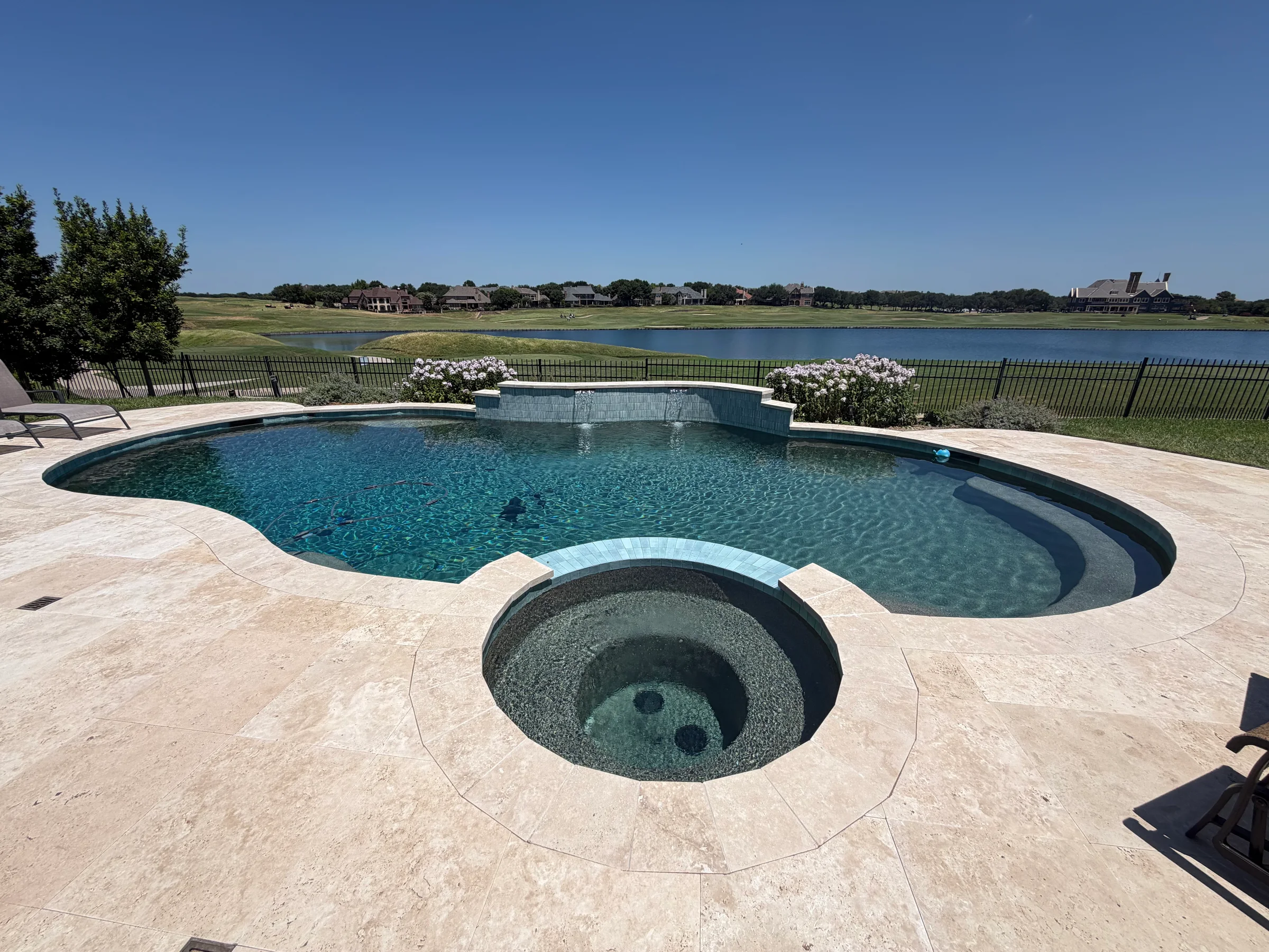 Completed residential swimming pool and spa with surrounding stone patio overlooking a waterfront landscape