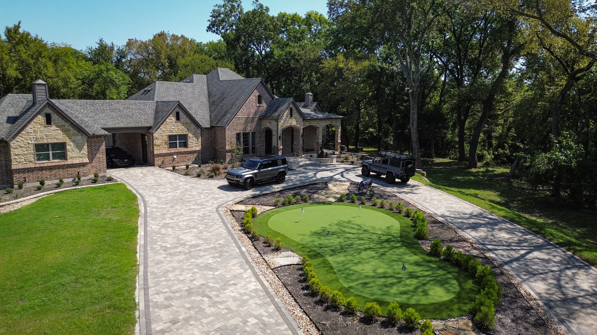 Broad paver motor court wrapping around an artificial-turf putting green