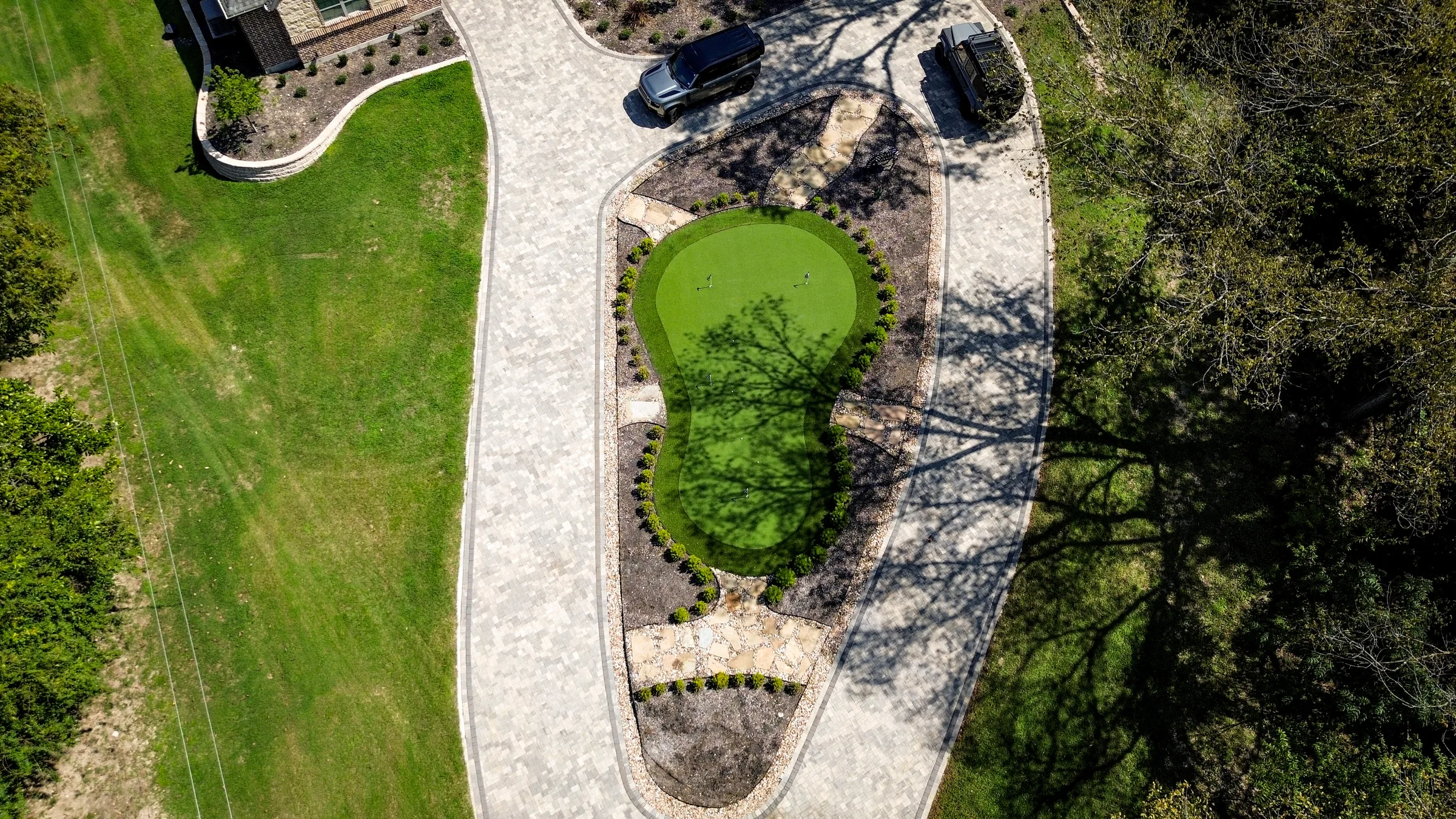 Aerial view of a putting green centered within a looping residential paver drive