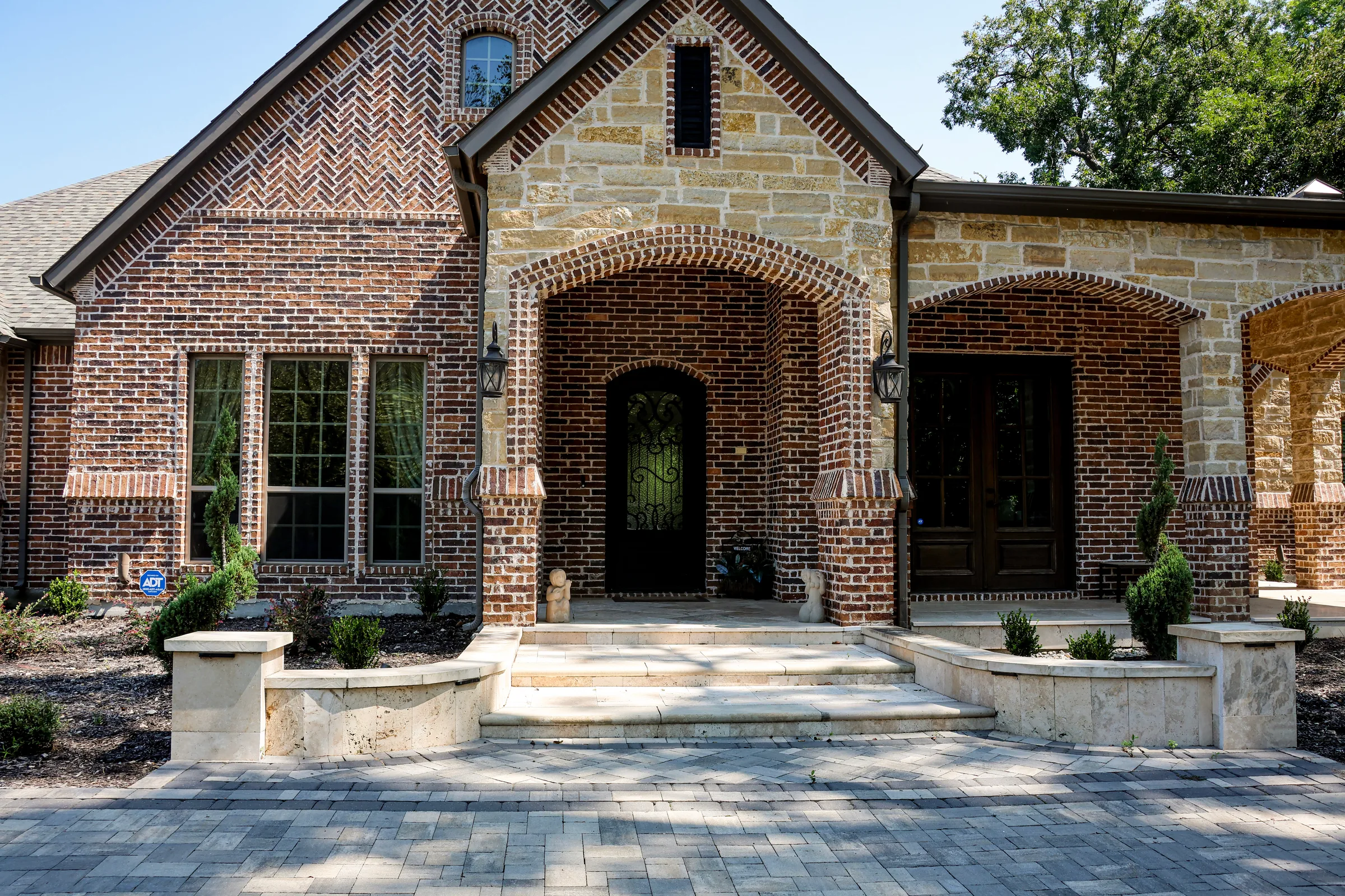 Light stone entry steps and a gray paver walk in front of a brick and stone home